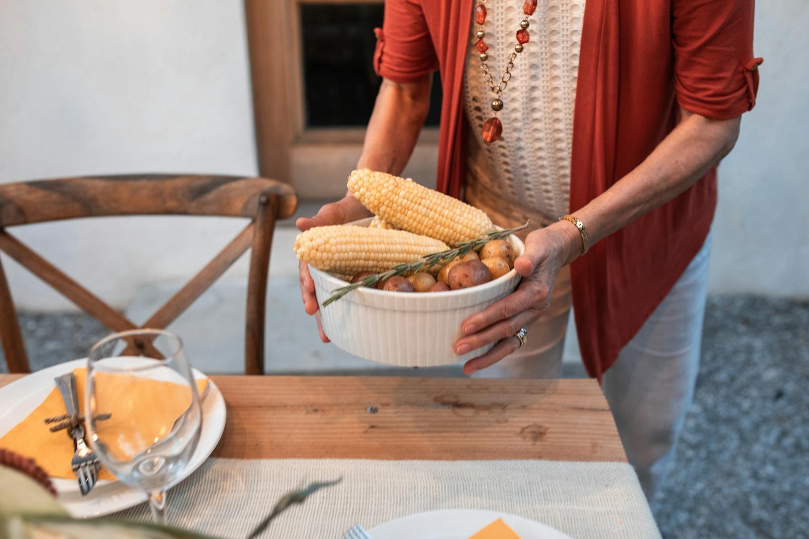 A woman sets a dinner table with corn and potatoes for a fall gathering.