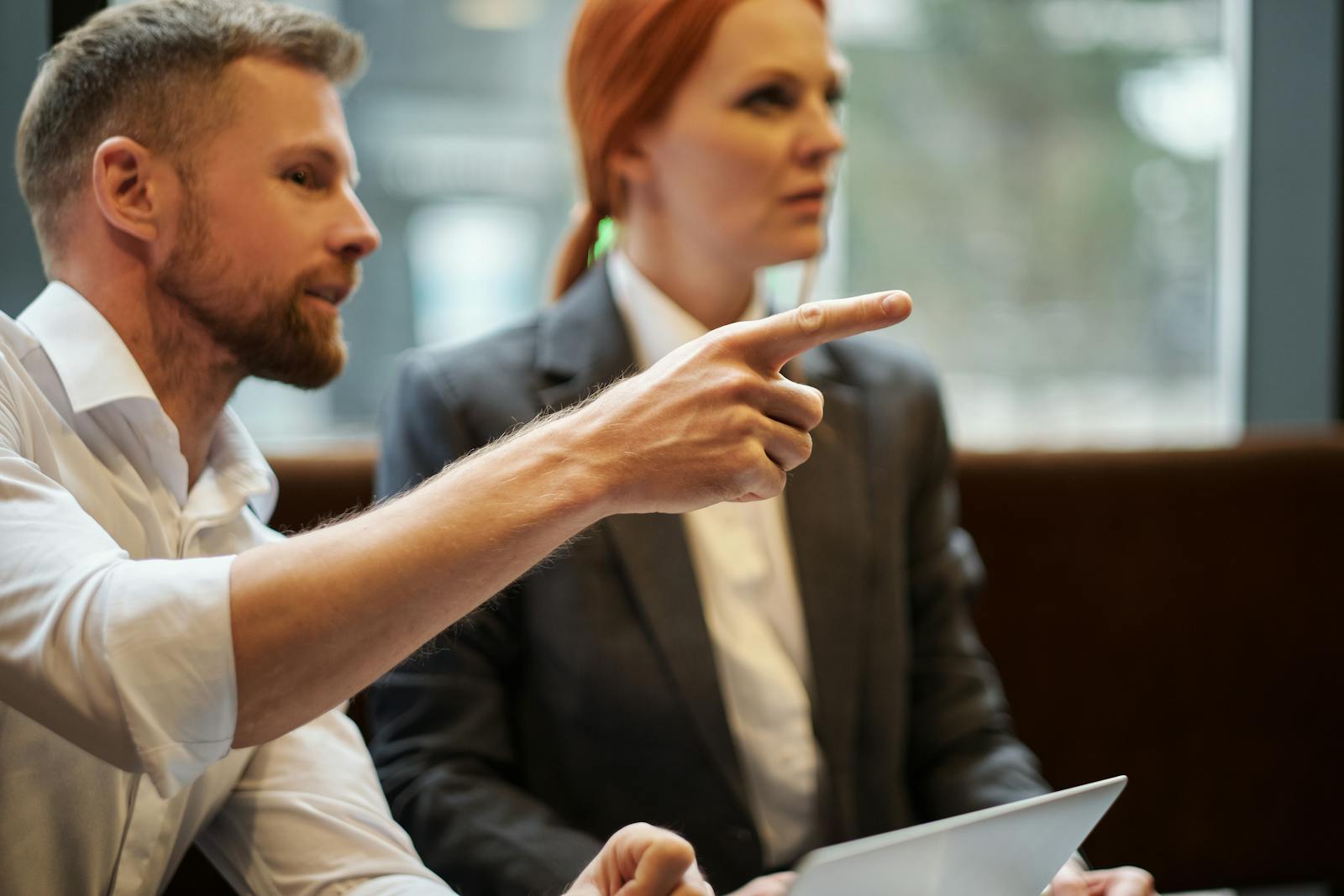 Focused business professionals in discussion, one pointing at an unseen item, captured indoors.