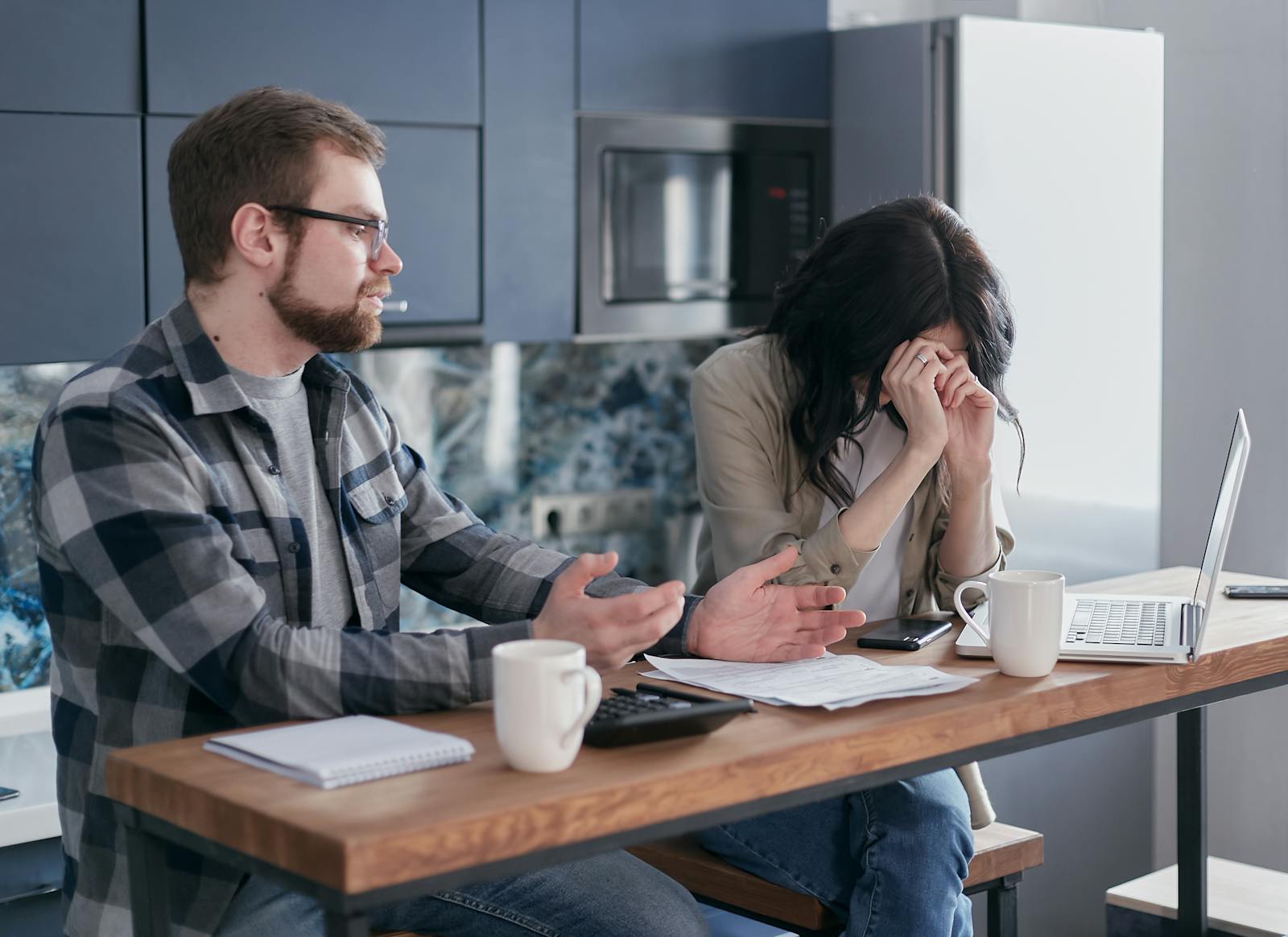A couple seated at a table, looking stressed while discussing financial issues indoors.