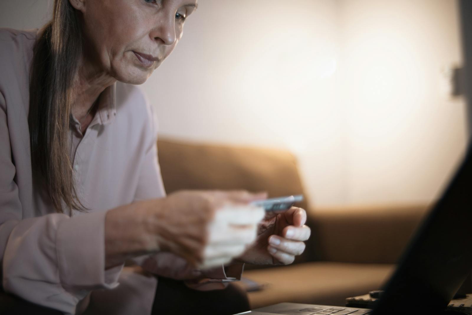 Senior woman using a laptop and credit card for online shopping in cozy home setting.