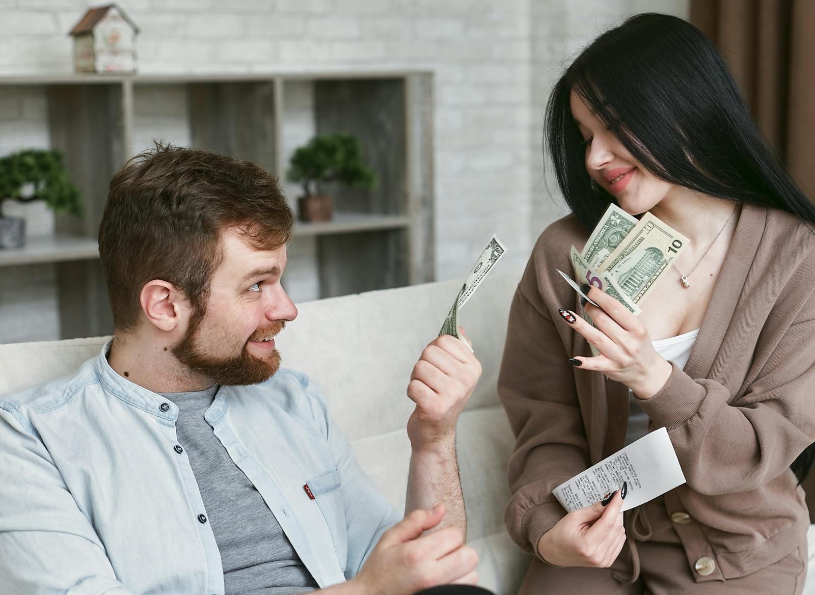 A cheerful couple managing their finances at home, holding cash and a receipt.