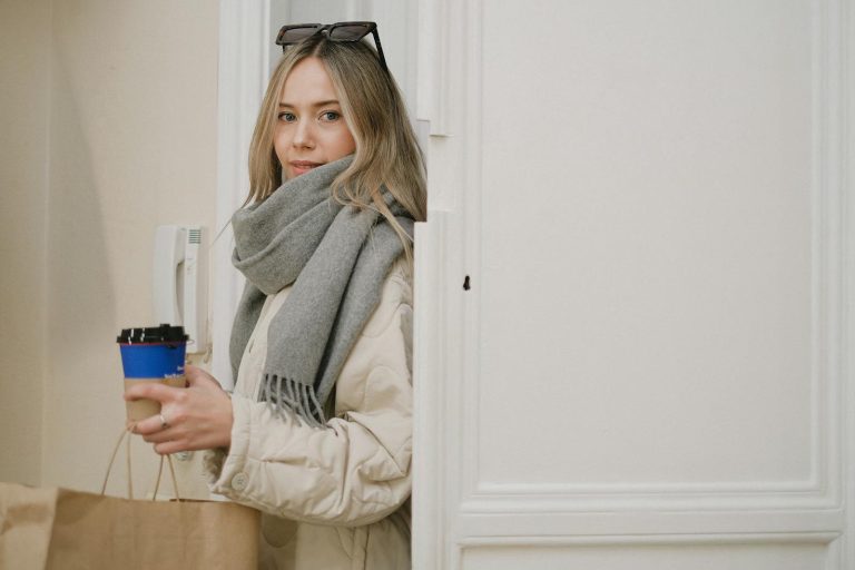 Caucasian woman indoors with coffee cup and shopping bag, dressed warmly in a scarf.
