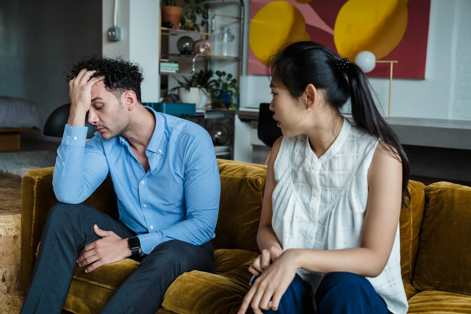 Upset couple in a heated discussion sitting together indoors on a sofa.