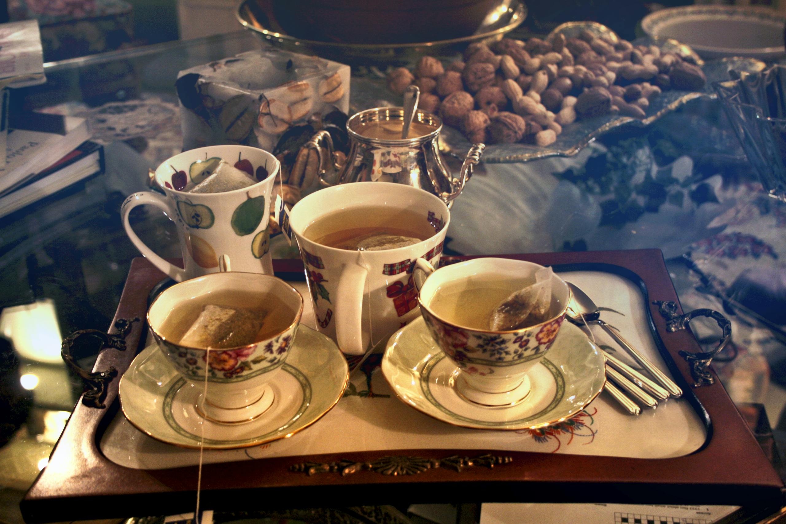 A warm setting with porcelain cups of tea on a tray, surrounded by nuts and elegant dishware.