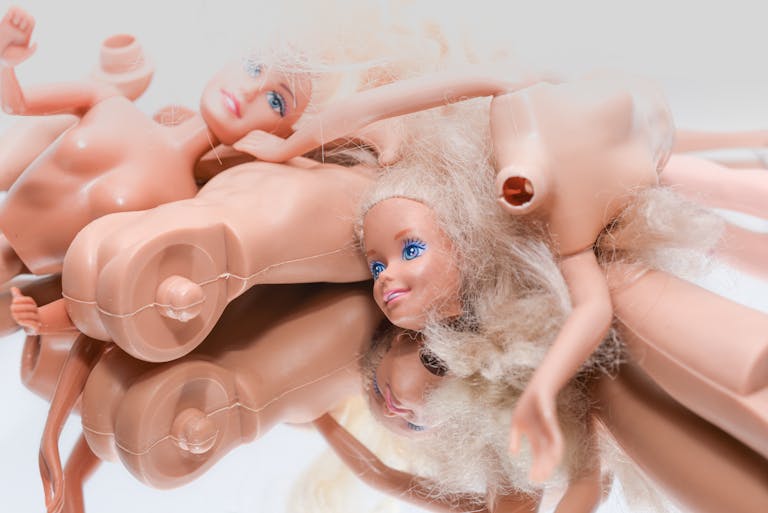 Artistic close-up of disassembled Barbie dolls with blonde hair indoors.