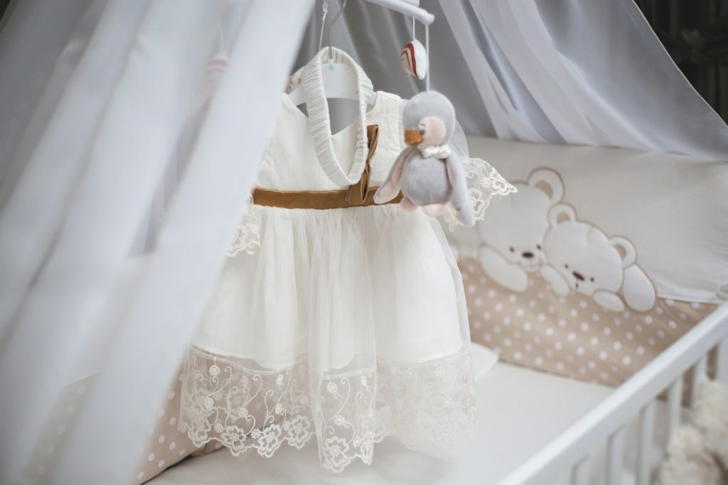 A delicate white baby dress hangs in a crib.
