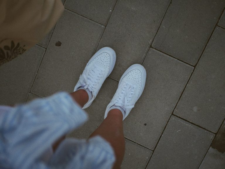 White sneakers on a person's feet walking on pavement.
