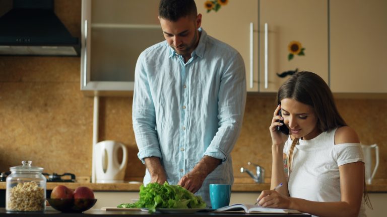 Man chopping vegetables while woman talks on phone