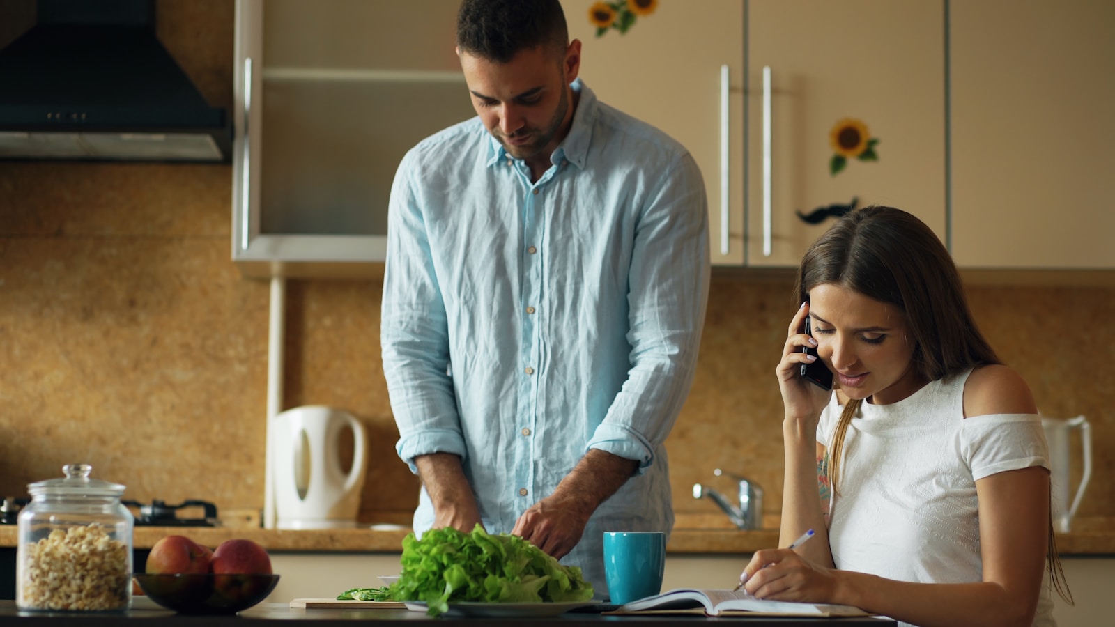 Man chopping vegetables while woman talks on phone