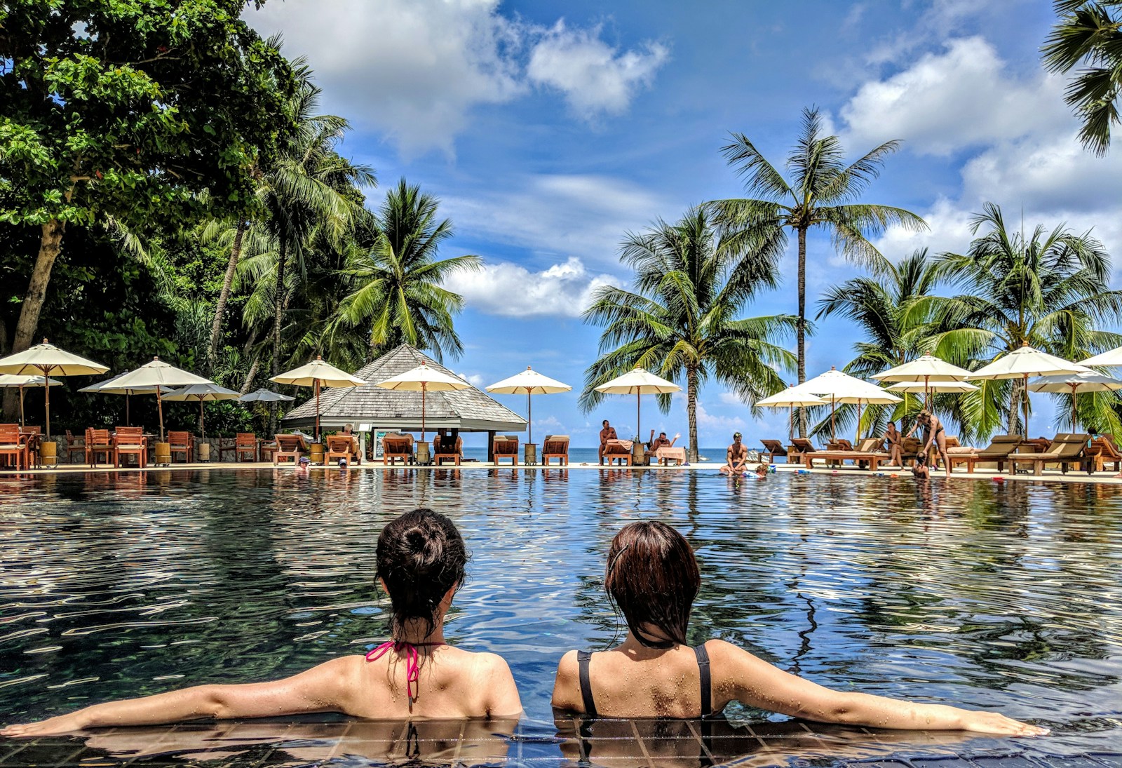 two woman leaning on inground pool tile