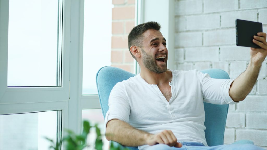 Man laughing while taking a selfie with tablet.