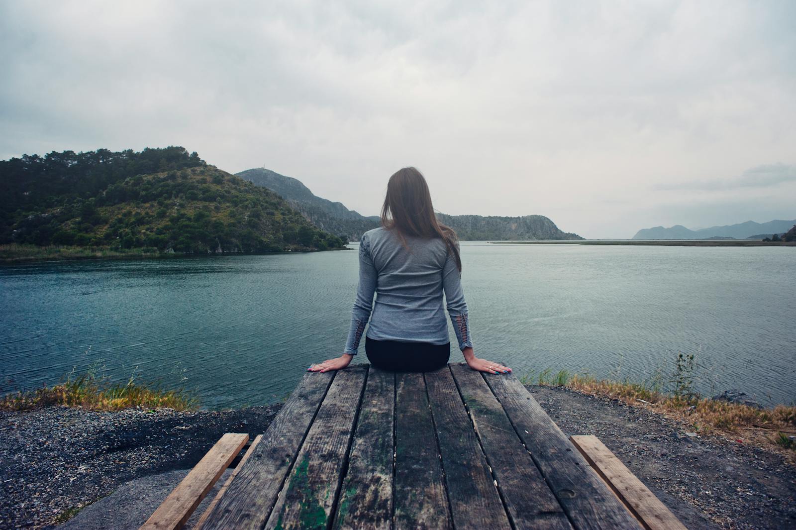 A woman sitting on wooden planks, enjoying a serene mountain lake view.