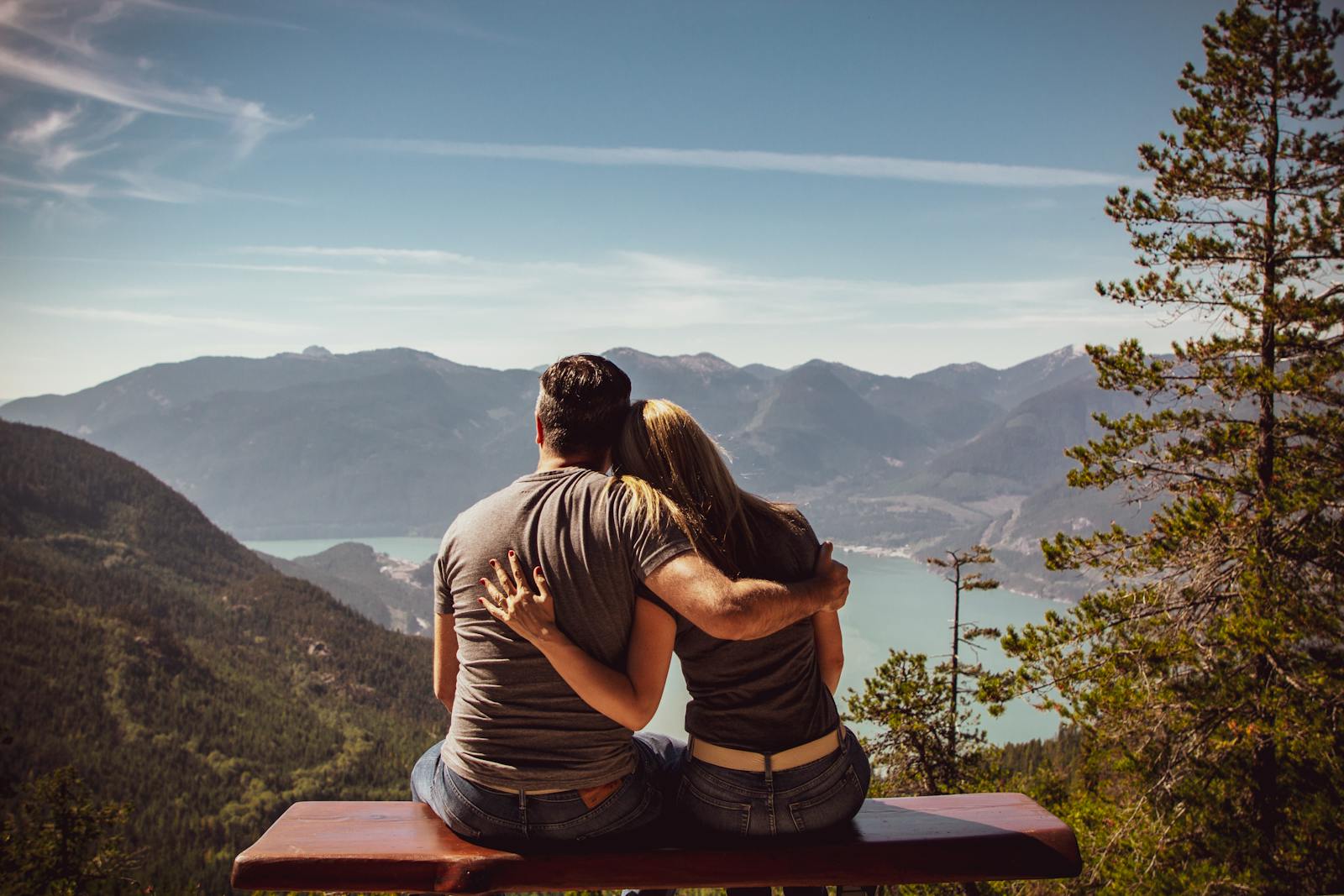 Couple sitting on bench embracing scenic mountain view, embodying romantic nature escape.