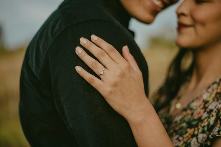 Romantic portrait of a couple showcasing an engagement ring in an intimate embrace outdoors.