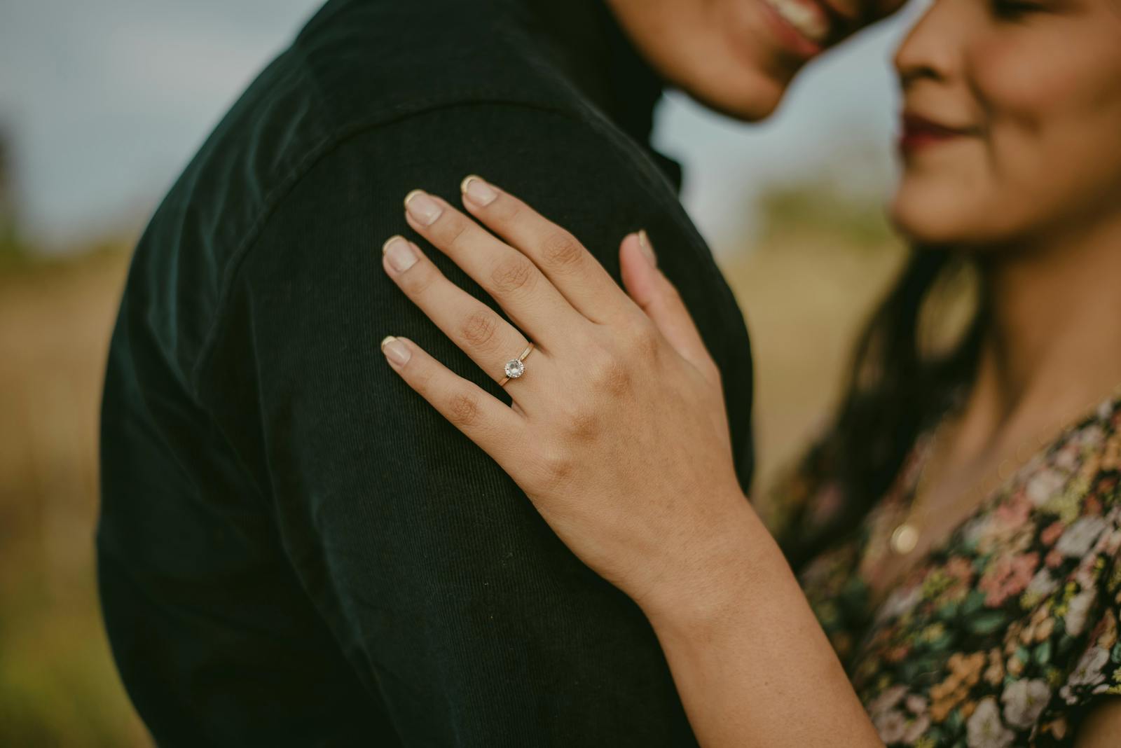 Romantic portrait of a couple showcasing an engagement ring in an intimate embrace outdoors.