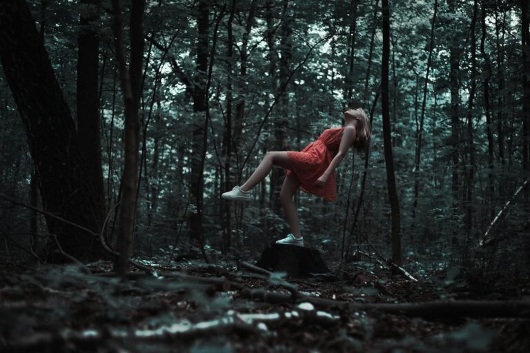 A woman in a red dress appears to levitate in a mysterious forest setting, evoking magic and creativity.