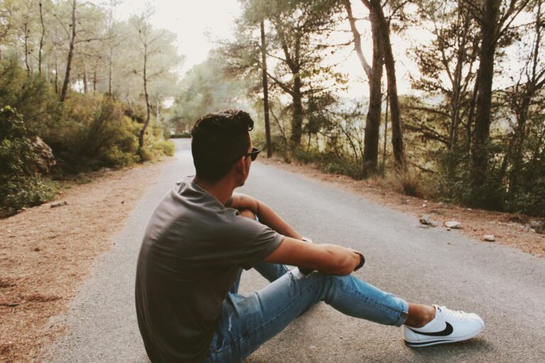 A young man sits on a forest road, enjoying solitude and nature's tranquility.