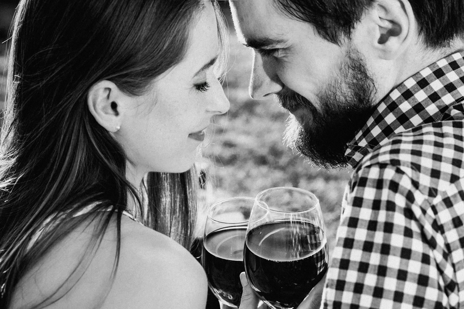 A romantic couple smiling and toasting with wine glasses outdoors, capturing a joyful moment.