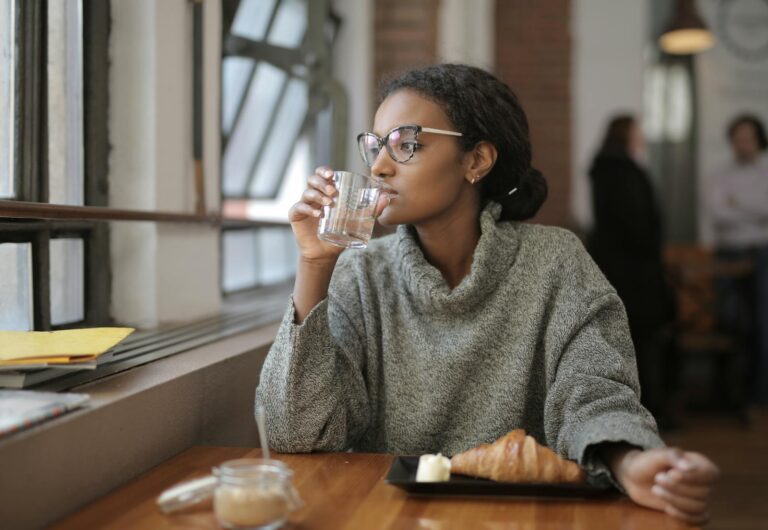 African American woman sipping water with a croissant at a cafe. Cozy indoor setting.