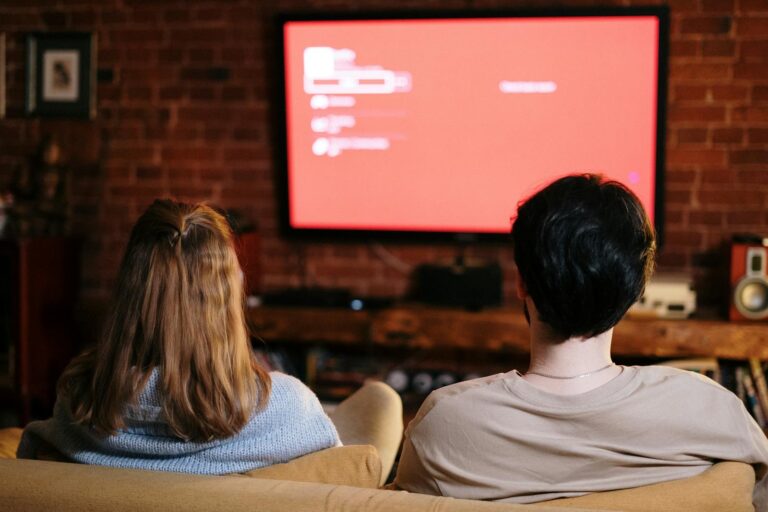 A couple watches TV together in a cozy brick-walled living room on a sofa.