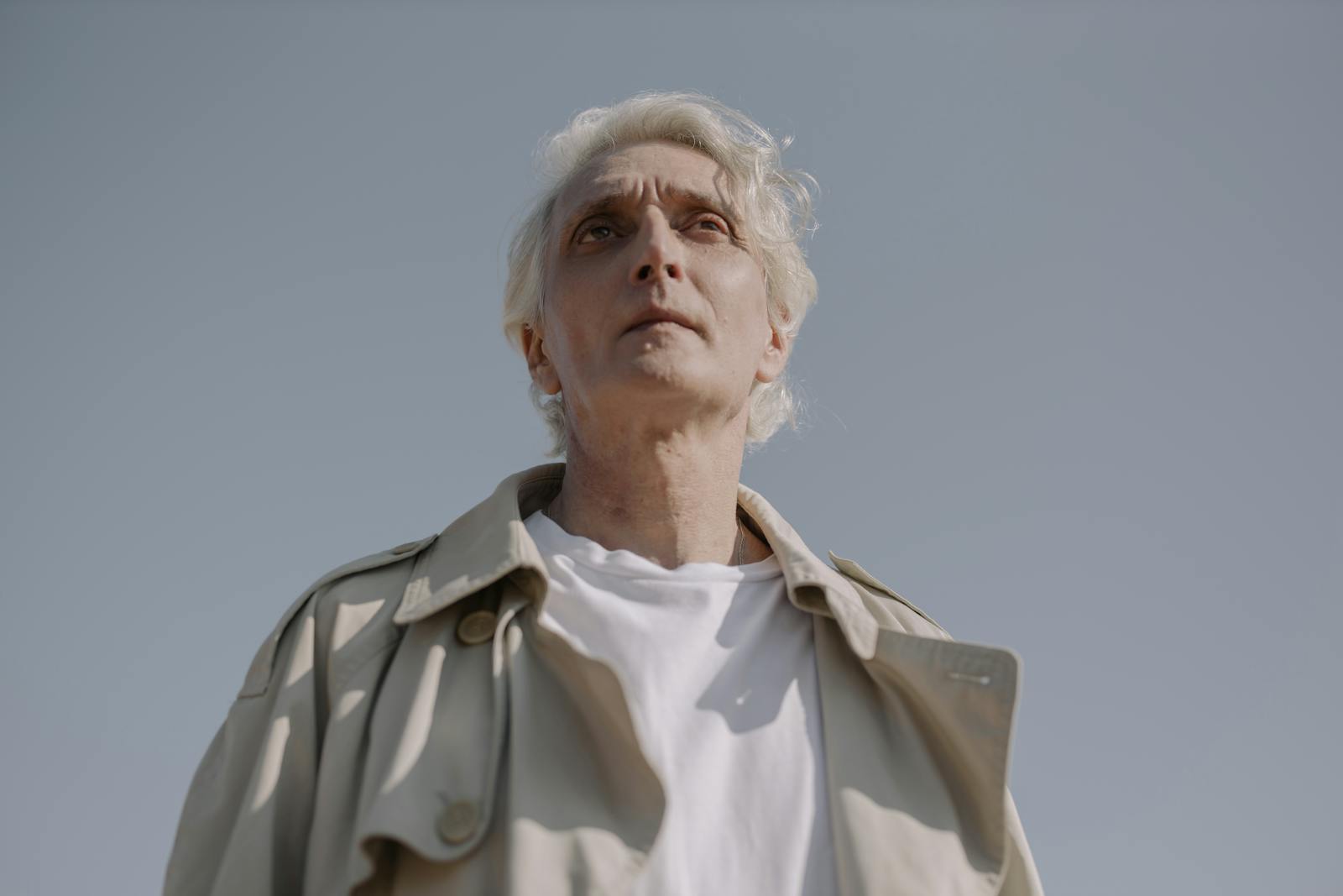 Low angle portrait of an elderly man in a grey coat against a clear sky, evoking serenity and wisdom.