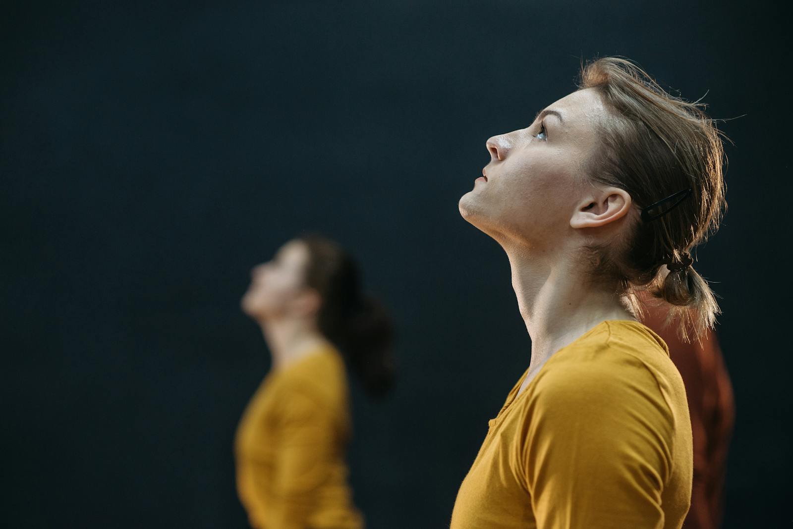 Side view of a woman in a yellow shirt looking upwards with a blurred background.