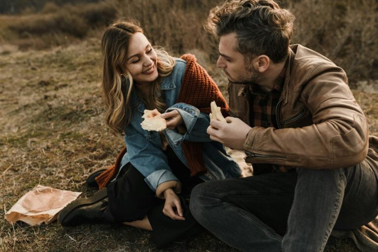 Happy couple enjoying a picnic outdoors, sharing bread and smiling warmly.