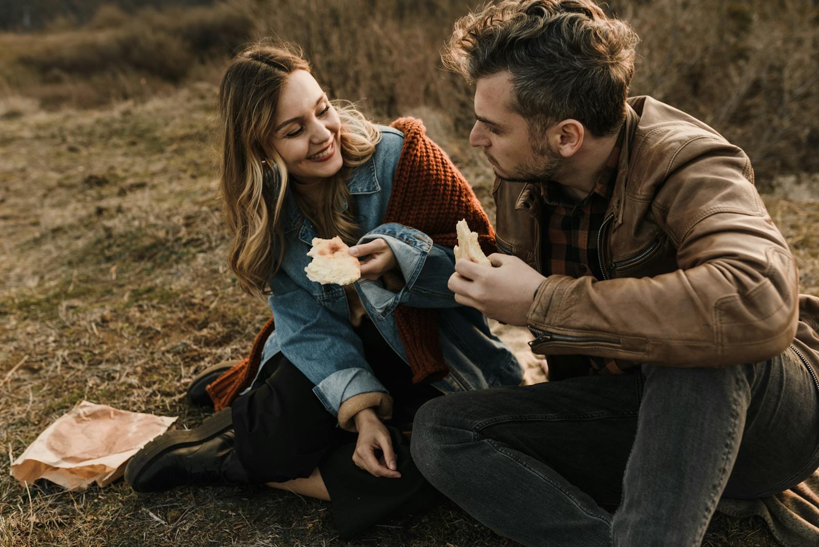 Happy couple enjoying a picnic outdoors, sharing bread and smiling warmly.