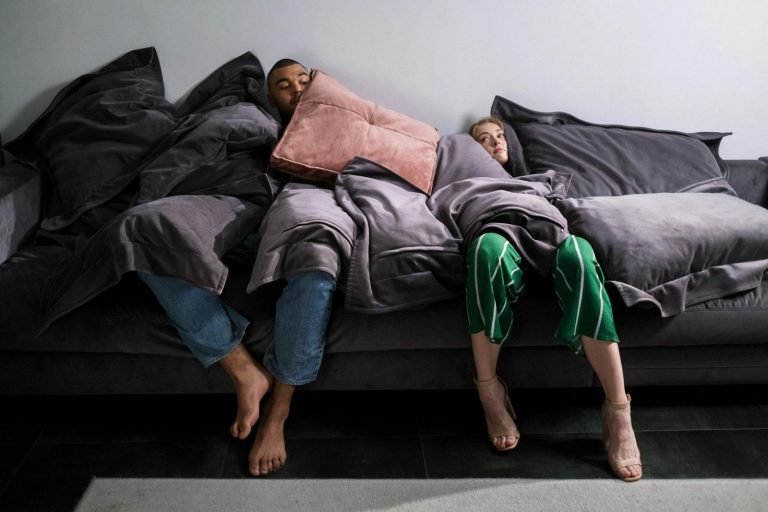 A diverse couple relaxes on a couch with pillows, embodying comfort and tranquility indoors.
