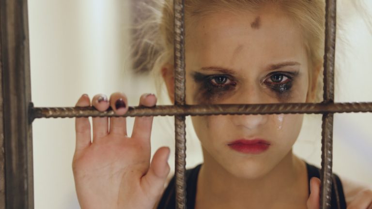 Sad young girl with smudged makeup behind bars
