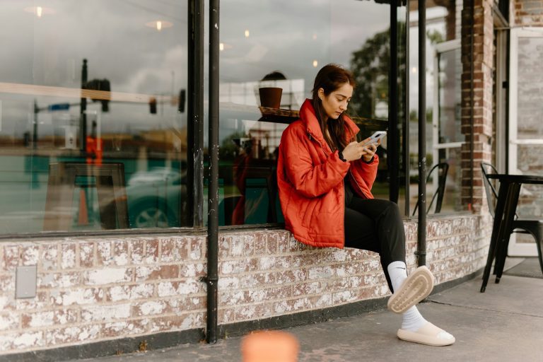 a woman sitting on a window sill looking at her cell phone