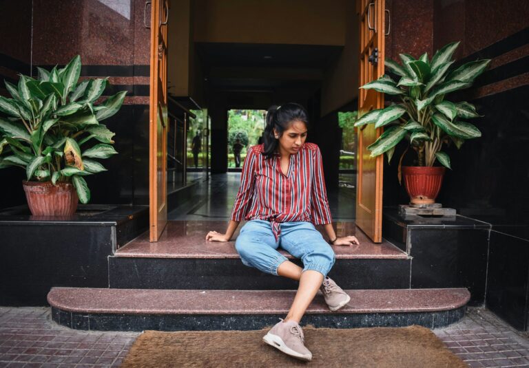 woman in pink and blue long sleeve shirt and blue denim jeans sitting on brown wooden