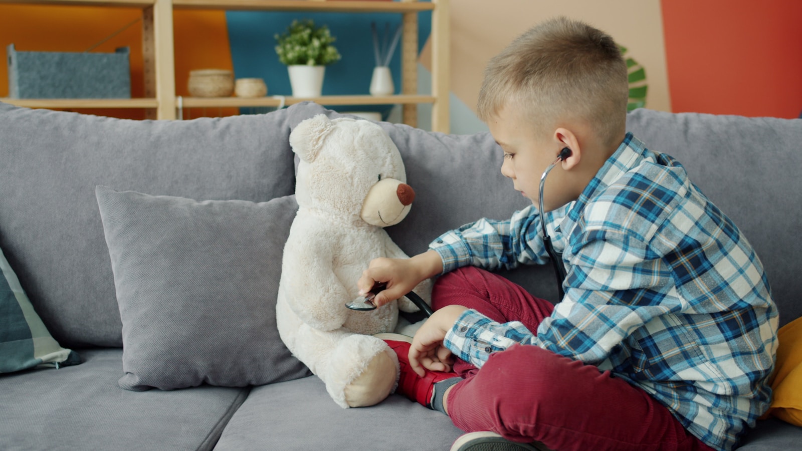 Boy listens to teddy bear with stethoscope on couch