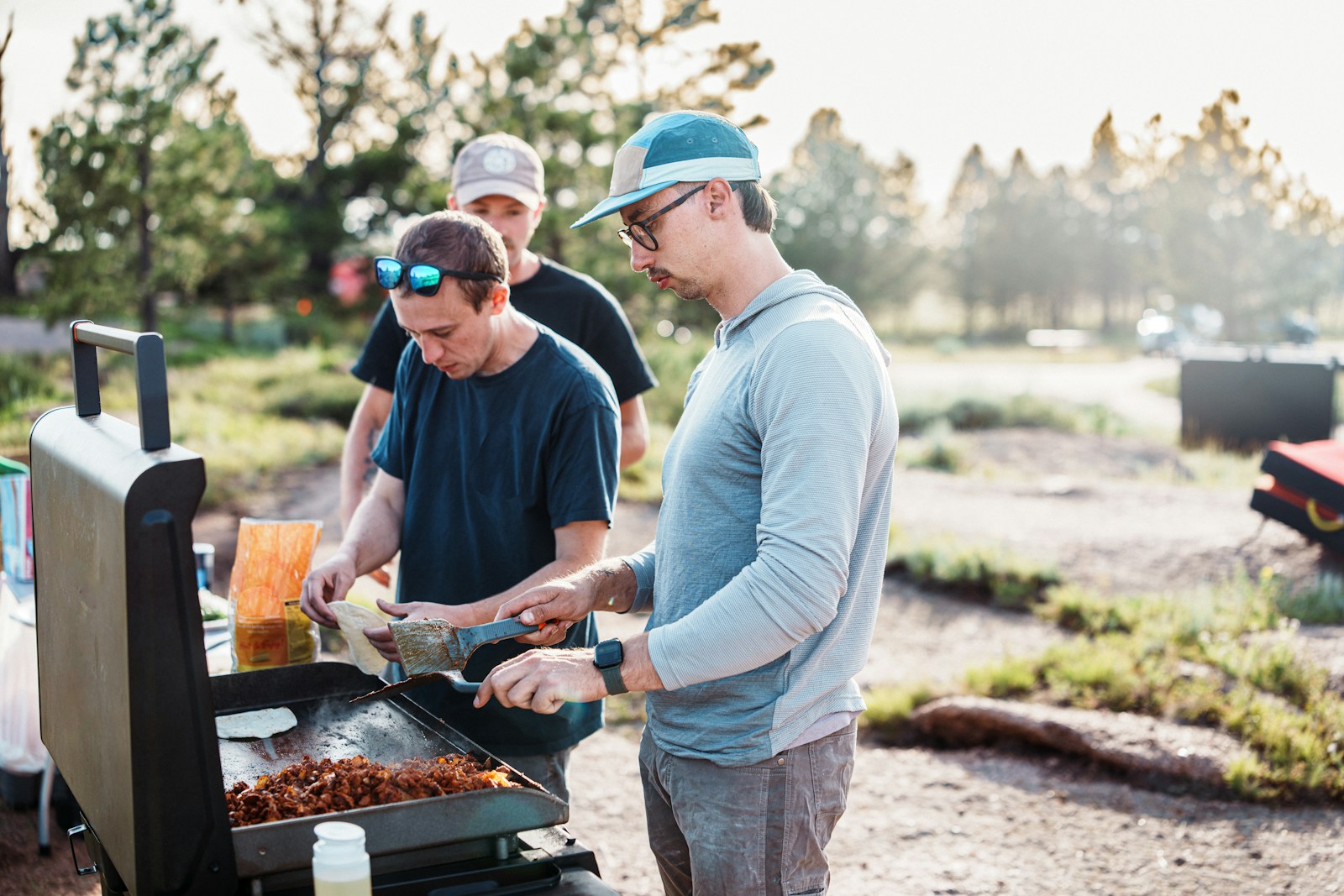 Three men cooking food on an outdoor grill.