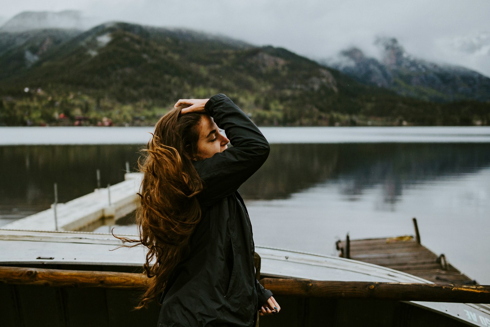 woman in black hoodie standing on brown wooden dock during daytime