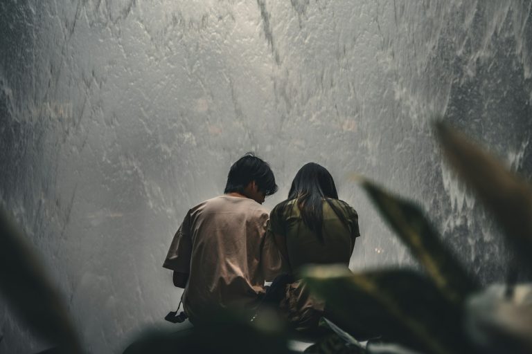 a man and a woman sitting on a bench looking at a waterfall