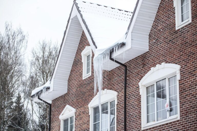 A brick house with snow-covered roof and icicles in a winter setting.