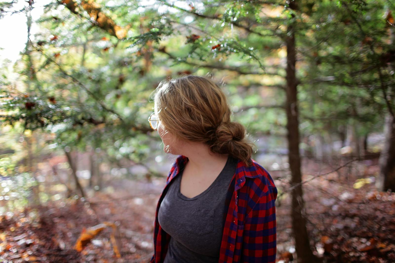 Woman hiking in a sunlit forest wearing casual attire, representing solitude and tranquility.