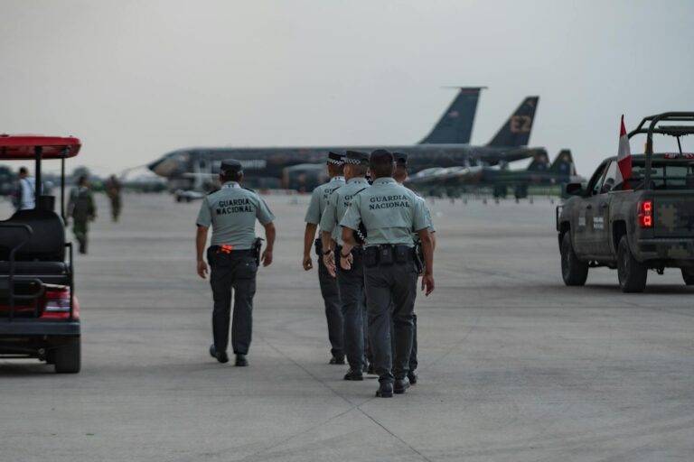 National Guard officers patrolling an airport tarmac with planes in the background.