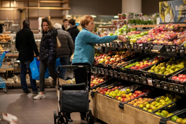Elderly woman using walker, shopping for fresh produce in Utrecht supermarket.