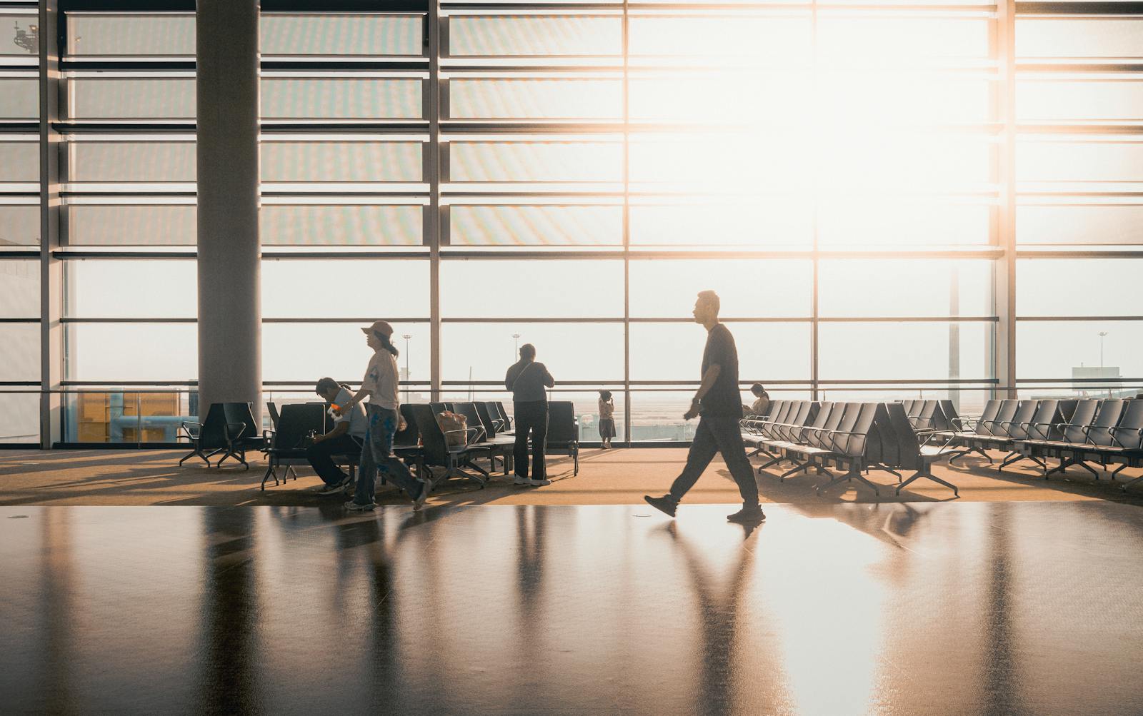 Silhouetted figures move through a sunlit Shanghai airport terminal, capturing travel's essence.