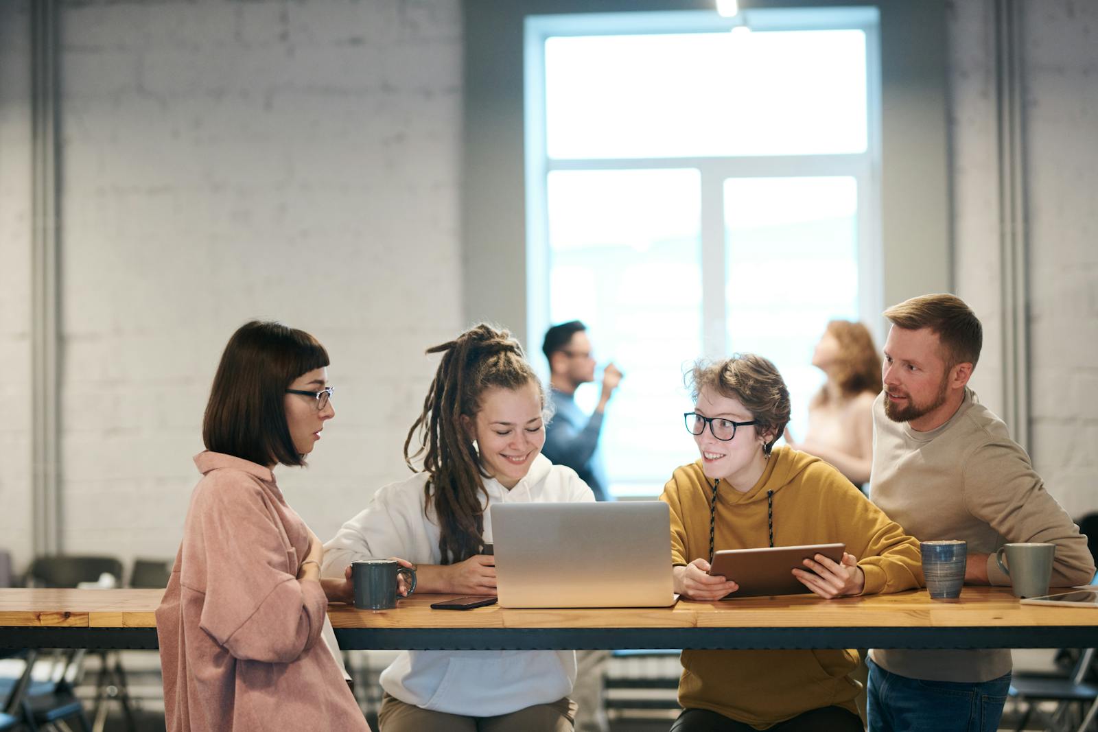 A group of young professionals collaborating indoors with laptops and tablets.