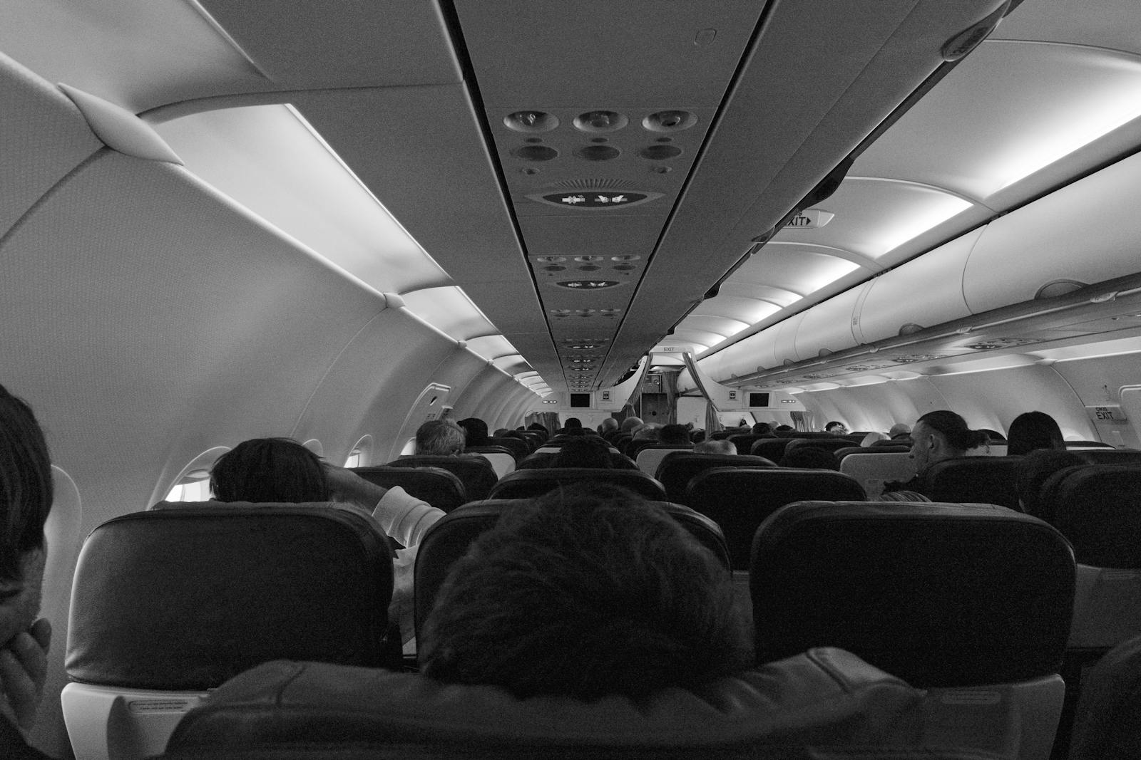 Black and white view of passengers seated inside an airplane cabin.