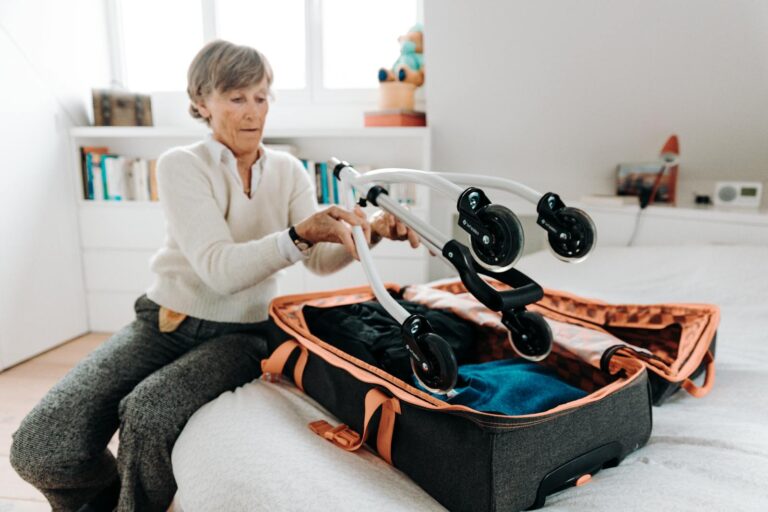 Senior woman packing a rollator into a suitcase indoors, preparing for travel.