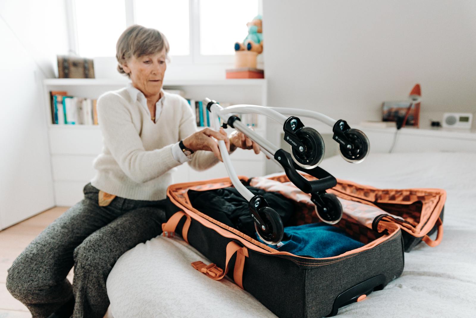Senior woman packing a rollator into a suitcase indoors, preparing for travel.