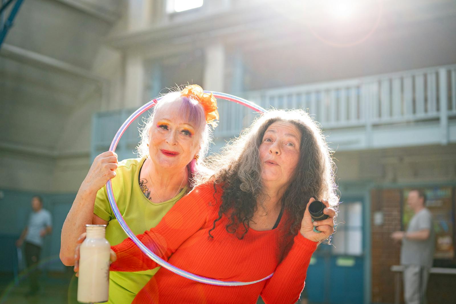 Two senior women enjoying a fun and lively exercise session with a hula hoop indoors.