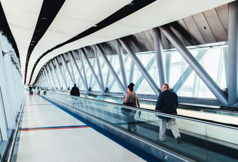 Travelers walking through a bright modern airport corridor with glass walls.