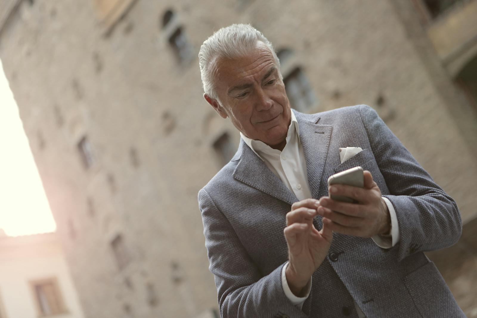 Senior man in a suit using a smartphone outside a historic building during the day.