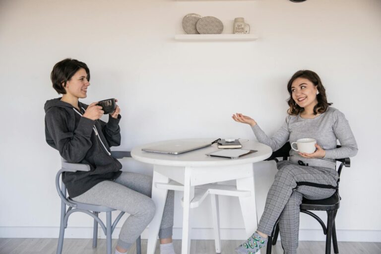 Two women enjoying a friendly chat over coffee indoors, relaxed and smiling.