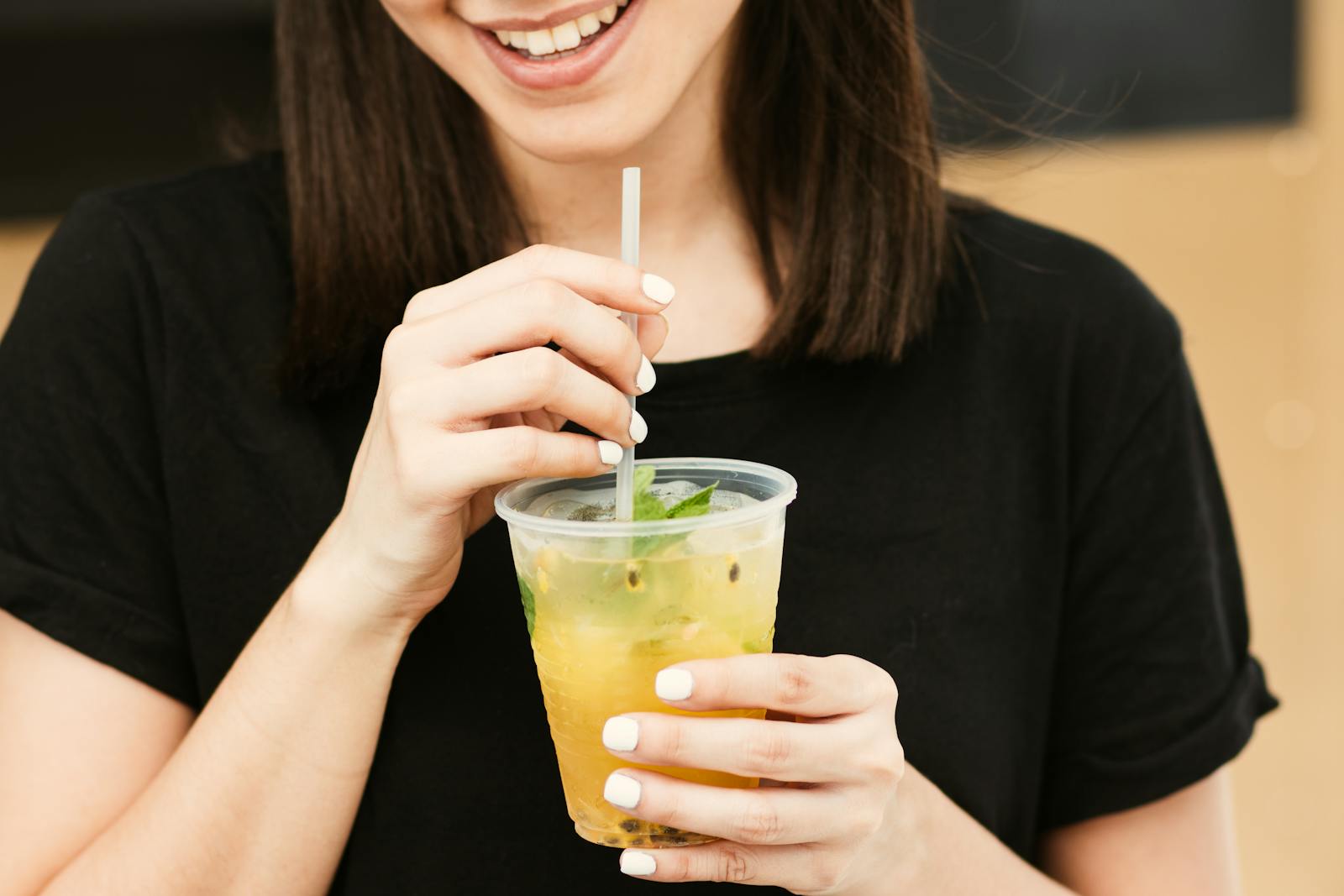 Woman enjoying a refreshing yellow drink through a straw with a smile.